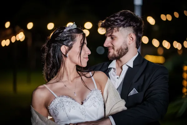 Novios abrazados de noche, con luces de fondo