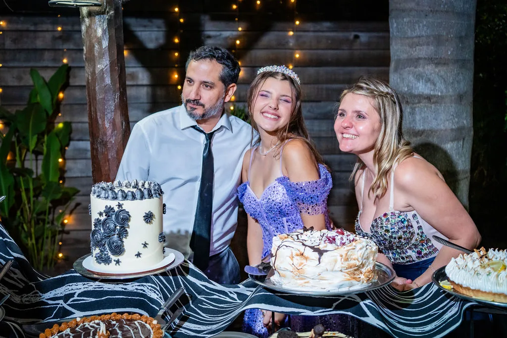 La quinceañera con sus papás frente a la mesa de las tortas
