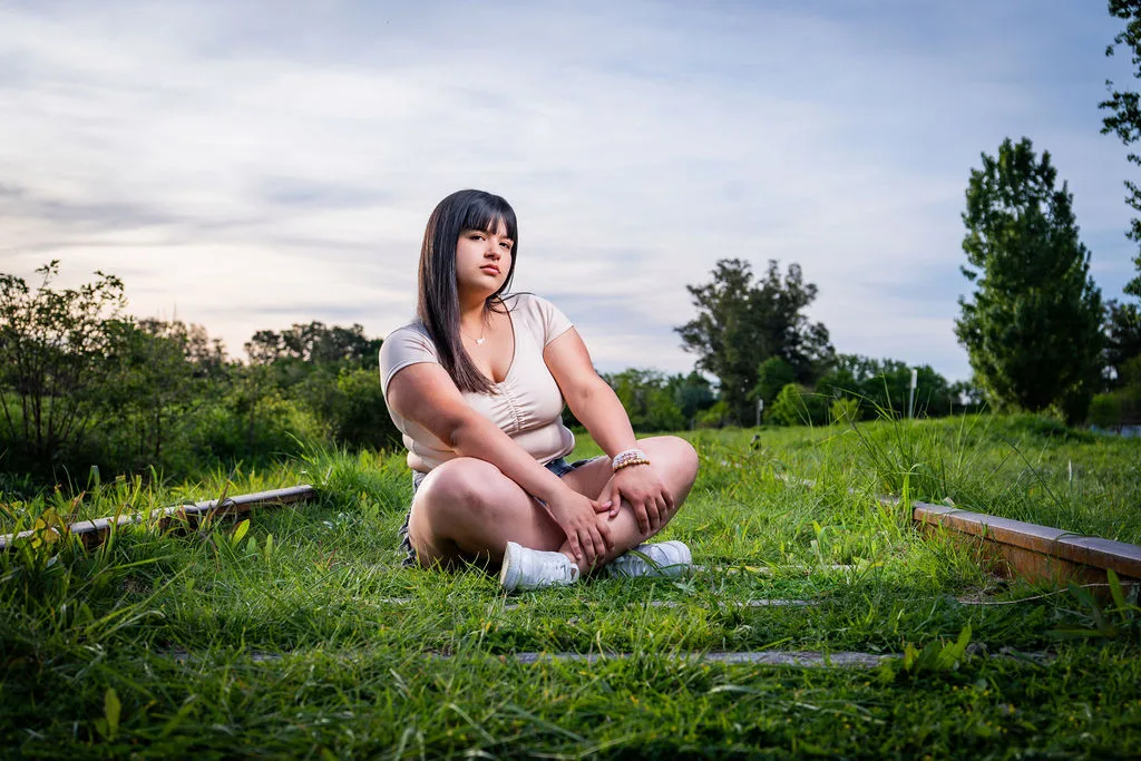 Quinceañera sentada en el pasto de un parque en un día nublado